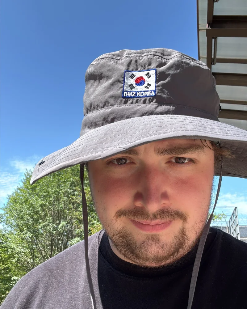 Justin Fresemann mit grauem Sonnenhut, auf dem Hut ein Aufnäher mit der südkoreanischen Flagge und „DMZ Korea“